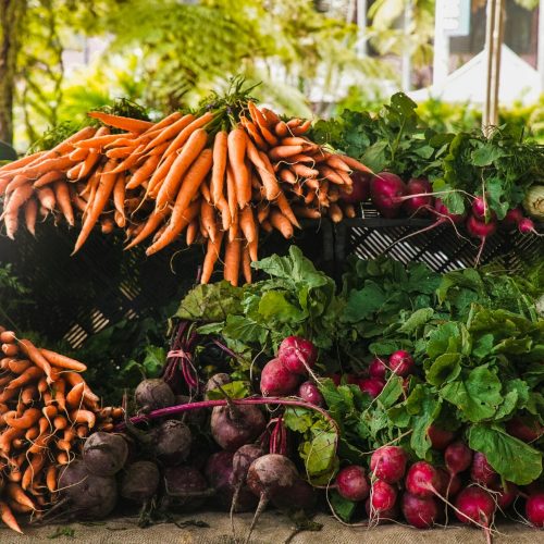 A vibrant display of fresh carrots, radishes, and greens at a local outdoor market.