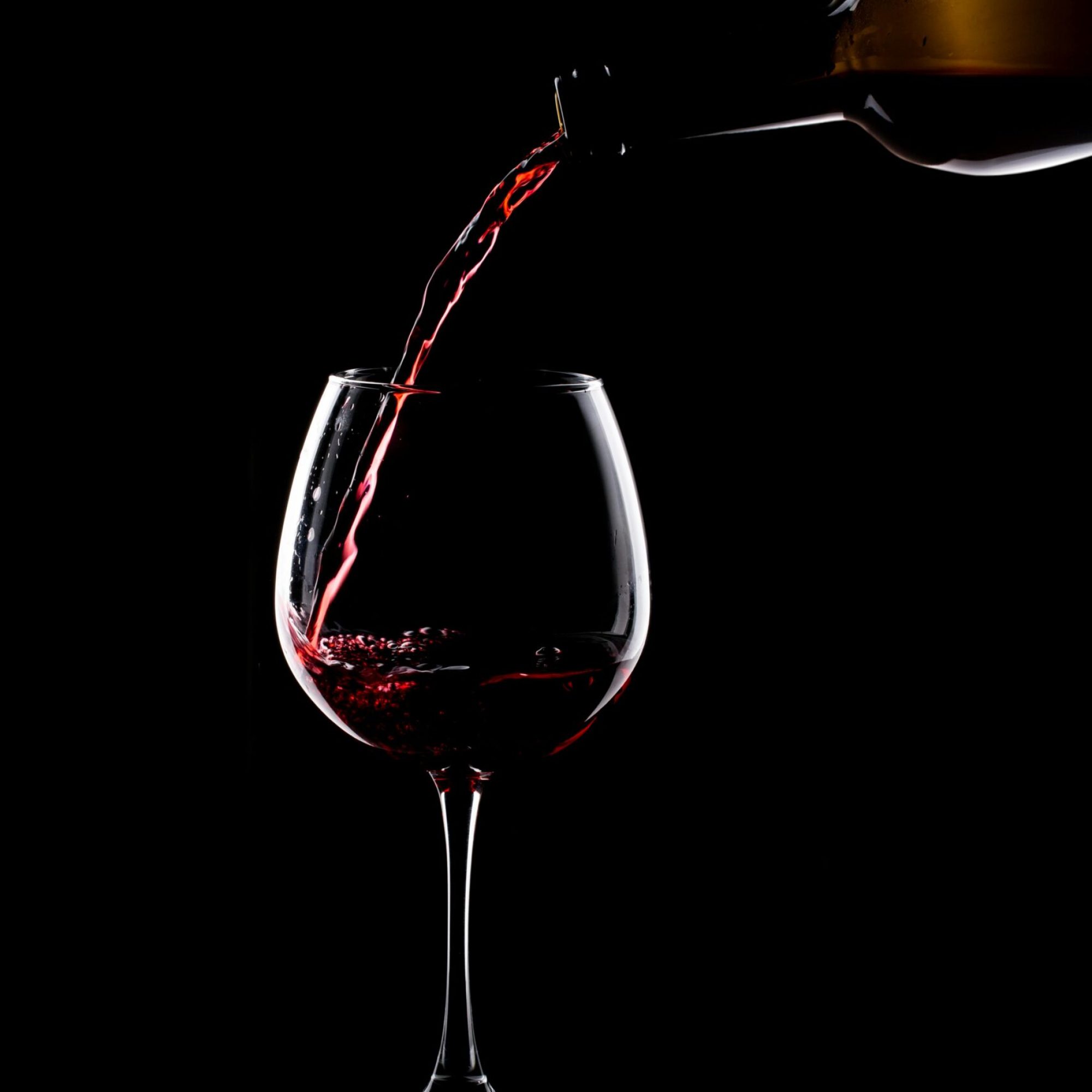 A stream of red wine poured into a glass on a black background, capturing elegance and sophistication.