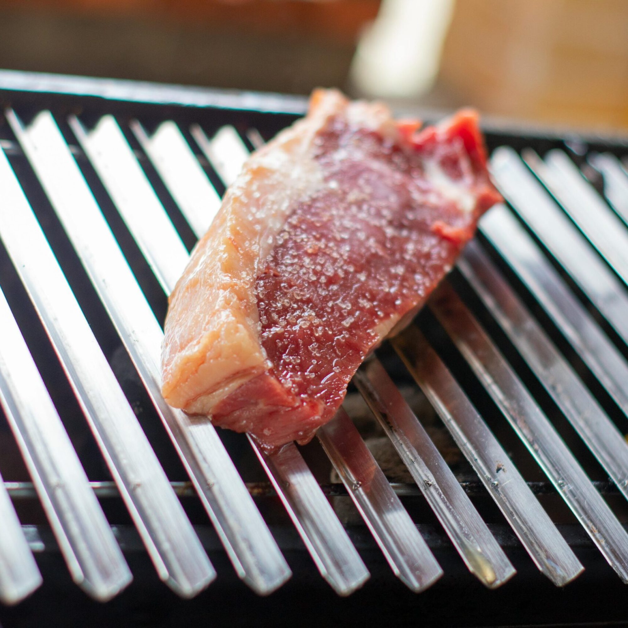 Close-up of a raw beef steak seasoned with salt on a grill grate in Recife, Brazil.